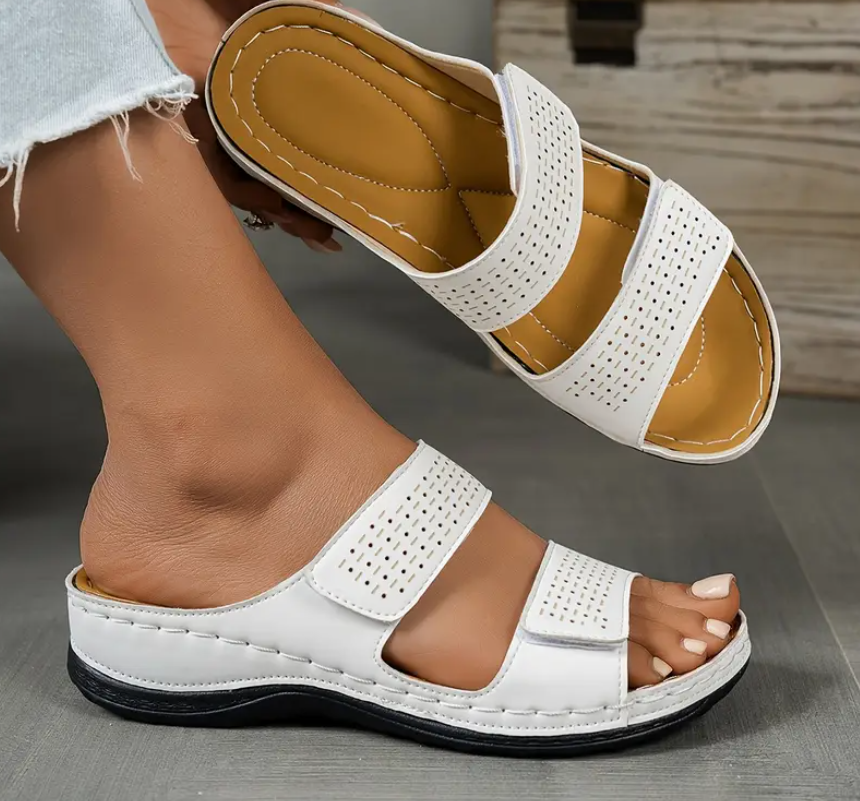 White sandals with brown soles worn by a person on a gray surface