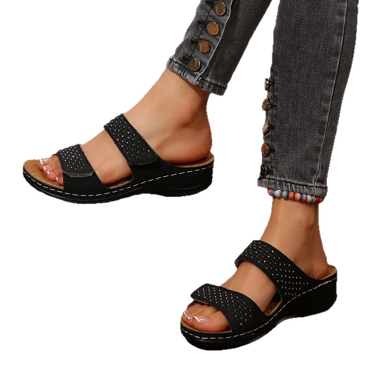 Black sandals worn with rolled-up jeans on a white background