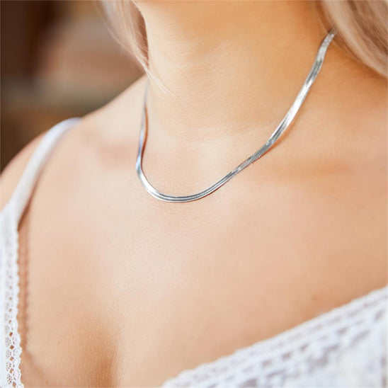 silver necklace on a person wearing a white top with a blurred background