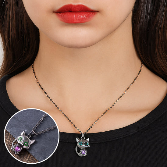 woman wearing a necklace with an owl pendant, close-up of the pendant on a black background.